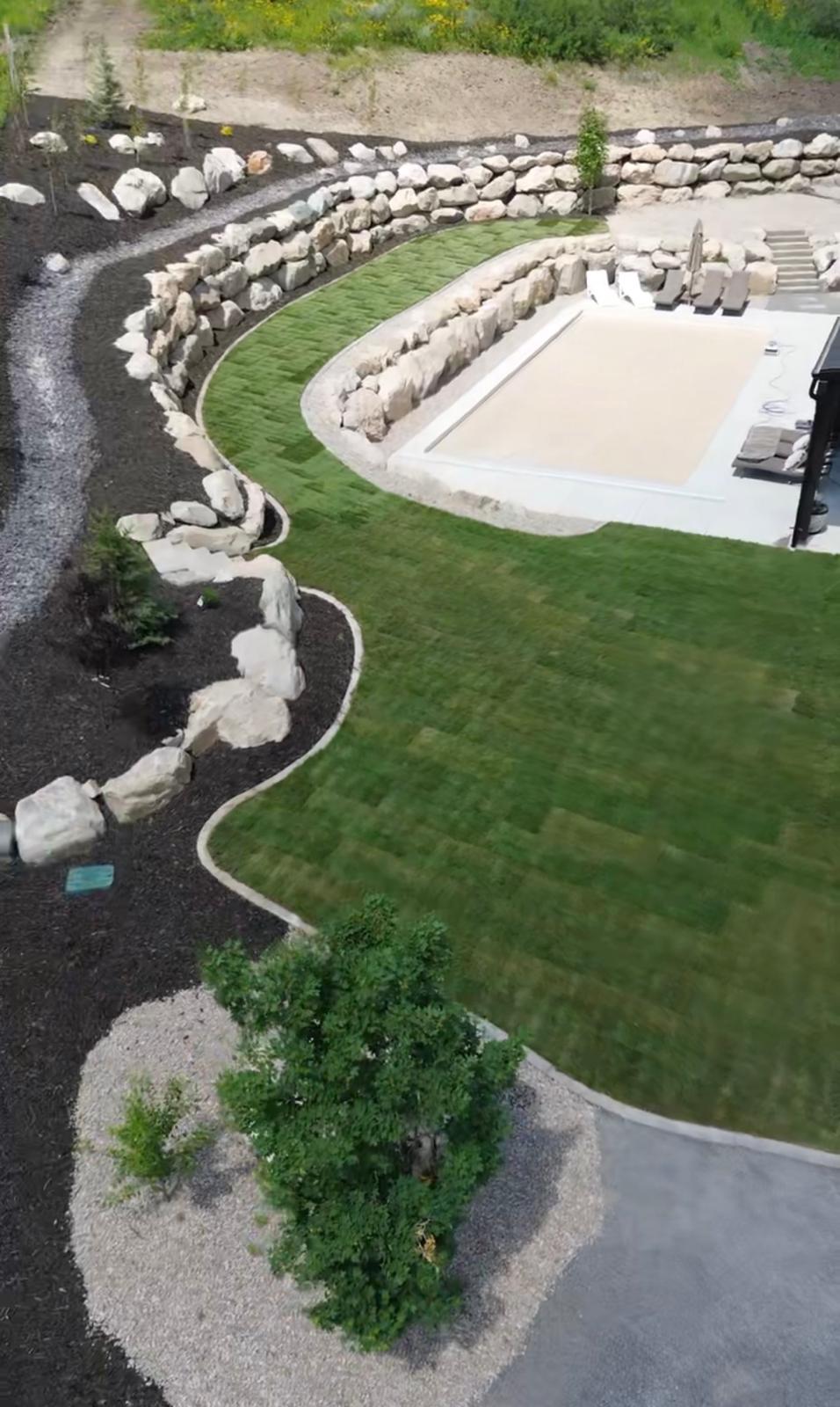 Aerial view of luxury backyard pool with engineered boulder retaining wall and full landscaping, Northern Utah estate